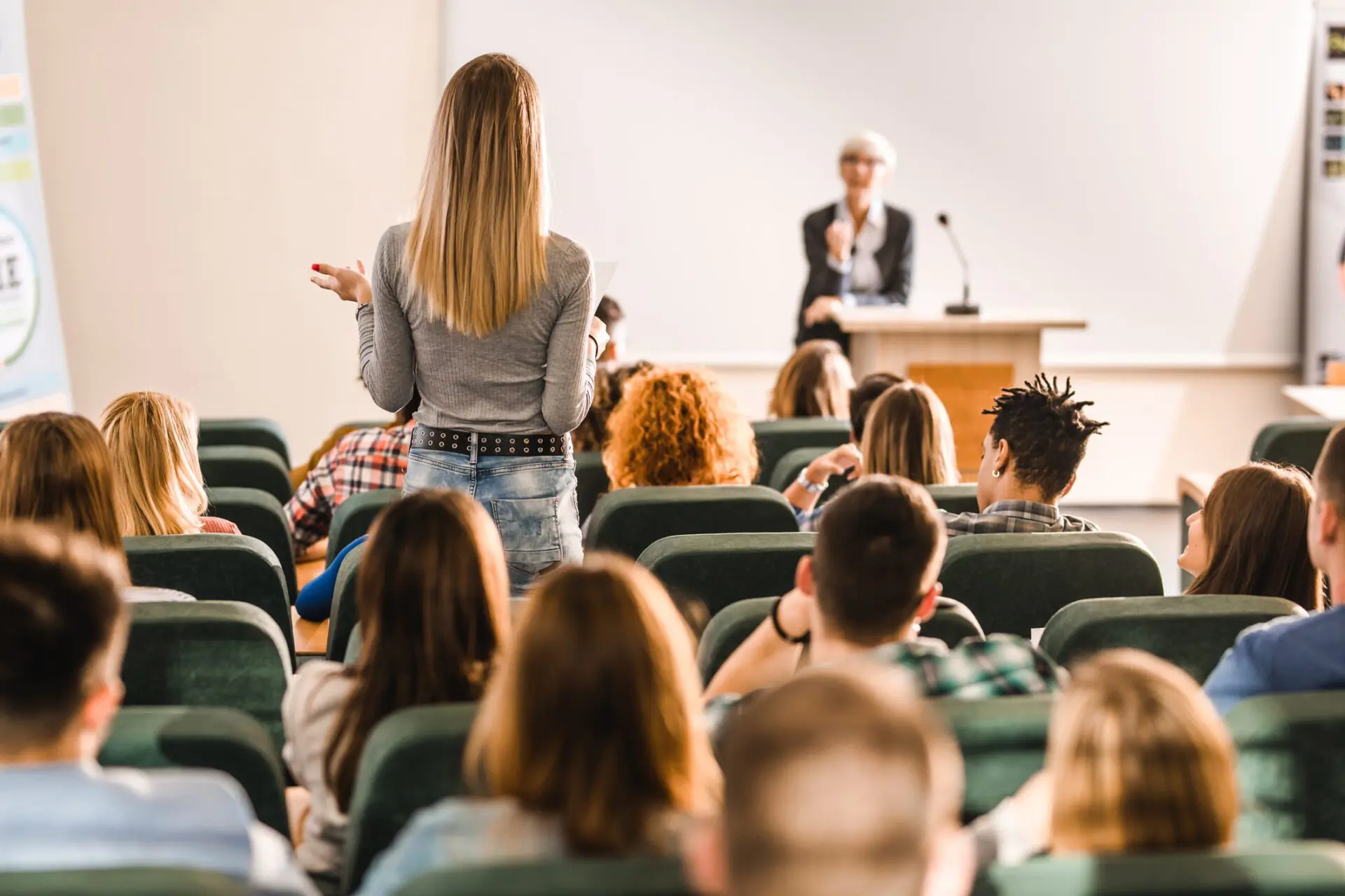 Back view of a female student talking to a professor on a class at lecture hall.